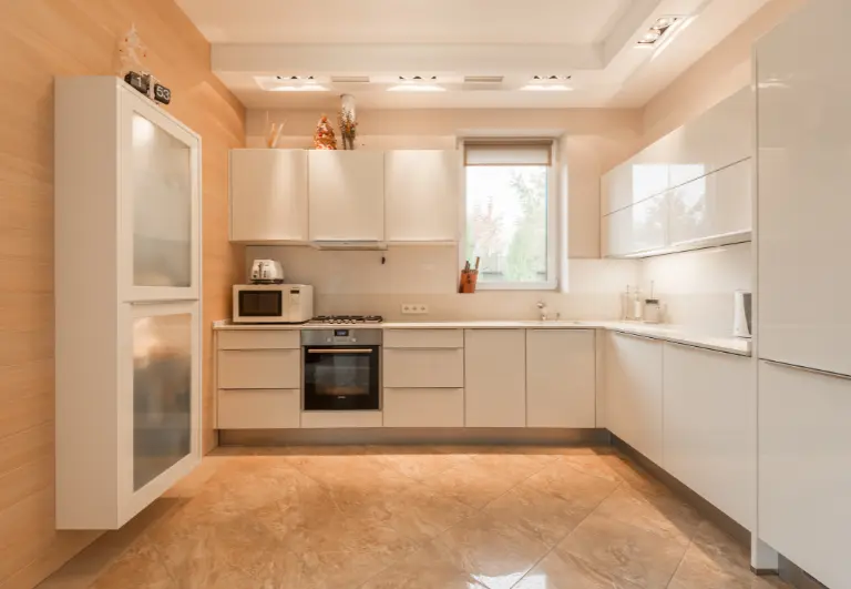 Vista frontal de una cocina modular económica en tonos blancos y madera, con módulos prefabricados y encimera integrada.