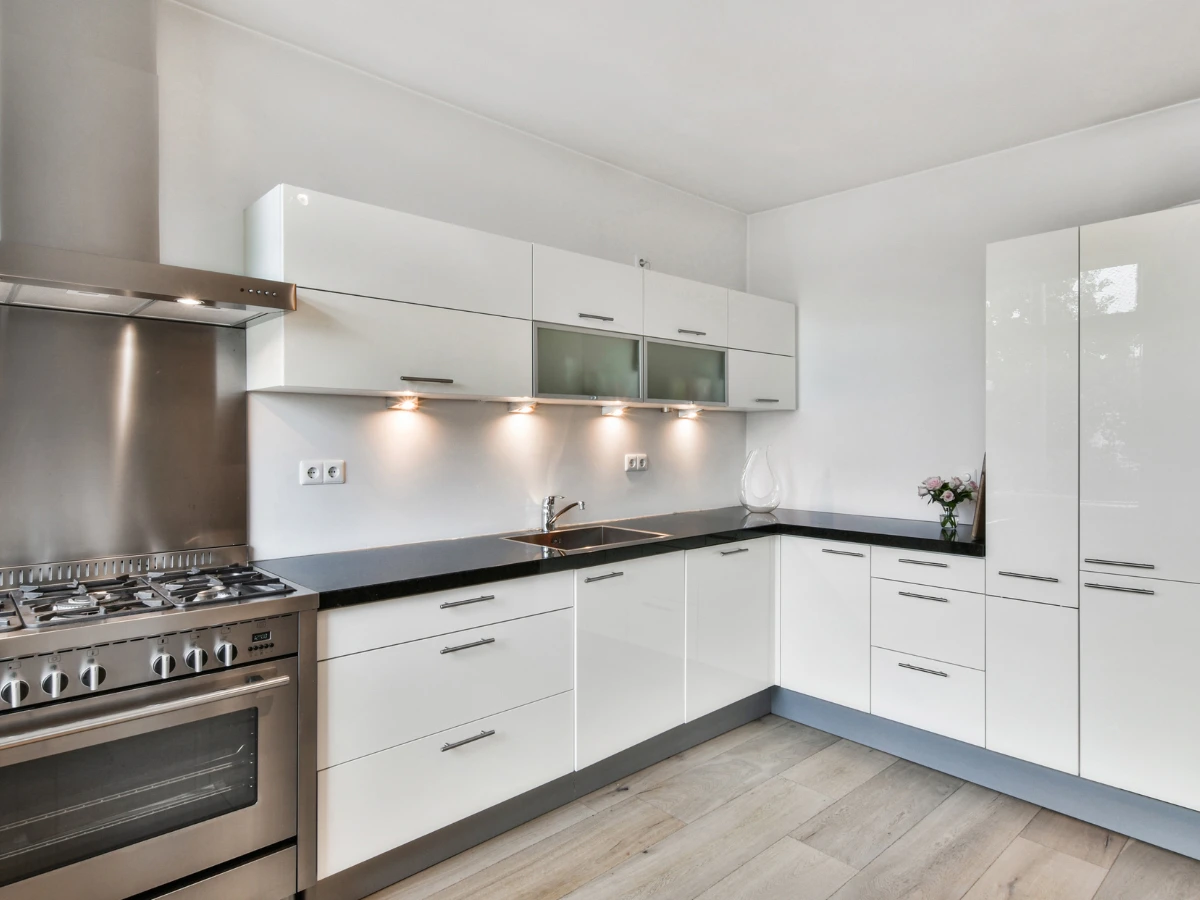Cocina moderna reformada en Barcelona con muebles blancos, encimera negra en L, electrodomésticos de acero y suelo de madera clara